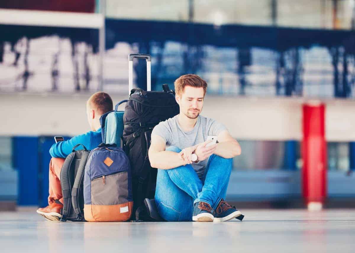 AdobeStock image of two travellers with mobile phones waiting at the airport departure area for their delay flight.