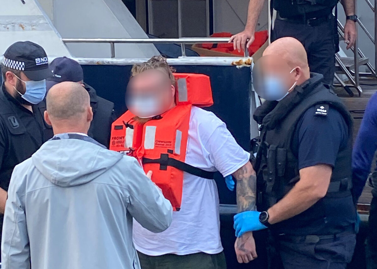 UK law enforcement officers leave the seized vessel with one of the arrested crewmen. Photo credit: AFP